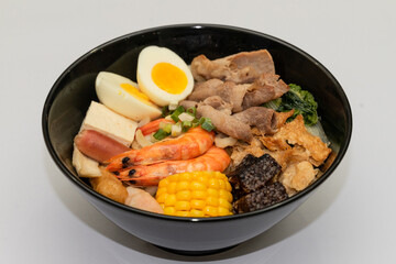 A hearty bowl of seafood noodle soup filled with shrimp, corn, egg, vegetables, rice blood cake, tofu skin, and assorted hotpot ingredients. The colorful ingredients float in a rich broth, making for 