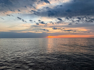 Colorful sunset over calm sea, dramatic clouds reflecting on the water, peaceful horizon and soft evening light create a serene and breathtaking ocean scene.