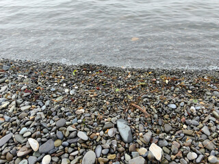 Pebble beach shoreline with small waves gently washing over smooth stones, natural textures and colors create a calm and peaceful coastal scene.