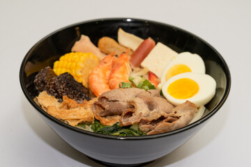 A hearty bowl of seafood noodle soup filled with shrimp, corn, egg, vegetables, rice blood cake, tofu skin, and assorted hotpot ingredients. The colorful ingredients float in a rich broth, making for 
