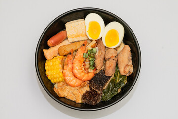 A hearty bowl of seafood noodle soup filled with shrimp, corn, egg, vegetables, rice blood cake, tofu skin, and assorted hotpot ingredients. The colorful ingredients float in a rich broth, making for 