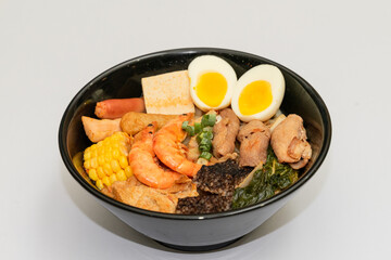 A hearty bowl of seafood noodle soup filled with shrimp, corn, egg, vegetables, rice blood cake, tofu skin, and assorted hotpot ingredients. The colorful ingredients float in a rich broth, making for 