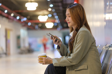 Businesswoman using smartphone during a break, seated on a bench with coffee in hand.
