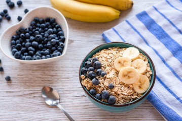 Porridge oatmeal with fresh fruit, a healthy breakfast bowl with oats, banana slices, and blueberries on a rustic wooden table.