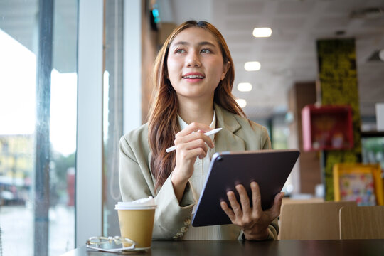Smiling businesswoman holding digital tablet and looking inspired during work at a cafe.