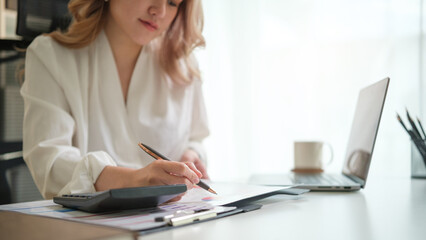 Businesswoman analyzing financial data and writing notes at her modern office desk.