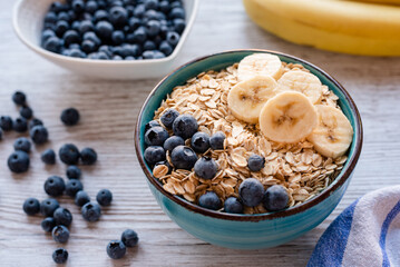 Porridge oatmeal with fresh fruit, a healthy breakfast bowl with oats, banana slices, and blueberries on a rustic wooden table.