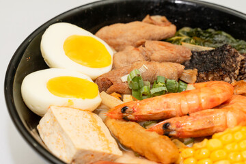 A hearty bowl of seafood noodle soup filled with shrimp, corn, egg, vegetables, rice blood cake, tofu skin, and assorted hotpot ingredients. The colorful ingredients float in a rich broth, making for 