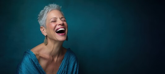 The joyful woman with short hair laughing against a teal backdrop.