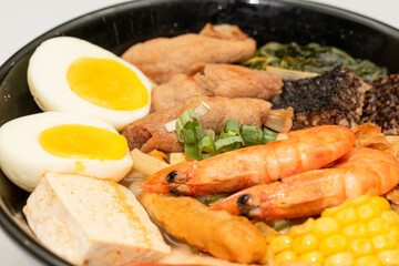 A hearty bowl of seafood noodle soup filled with shrimp, corn, egg, vegetables, rice blood cake, tofu skin, and assorted hotpot ingredients. The colorful ingredients float in a rich broth, making for 