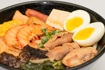 A hearty bowl of seafood noodle soup filled with shrimp, corn, egg, vegetables, rice blood cake, tofu skin, and assorted hotpot ingredients. The colorful ingredients float in a rich broth, making for 