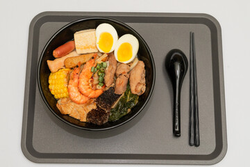 A hearty bowl of seafood noodle soup filled with shrimp, corn, egg, vegetables, rice blood cake, tofu skin, and assorted hotpot ingredients. The colorful ingredients float in a rich broth, making for 