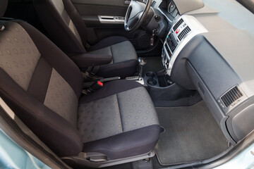 Fototapeta premium Comfortable front seats inside the car: the driver and passenger, tied with black fabric trim, modern interior design, the steering wheel covered and a luxurious center console.