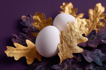 Two white eggs nestled among gold-leafed and purple-painted oak leaves on a deep purple background