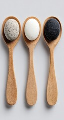 Three wooden spoons, each holding a spherical object ? light gray speckled, white, and dark gray