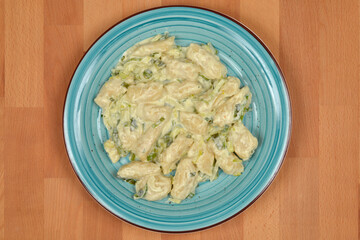 A generous serving of homemade gnocchi in a creamy leek sauce is presented on a textured blue plate, centered on a warm wooden background