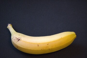 Single banana on black background with copy space. Close-up of tropical fruit with bold contrast.