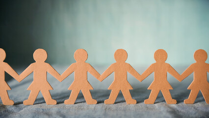 Paper chain of female figures holding hands on a textured surface against a blurred background scene
