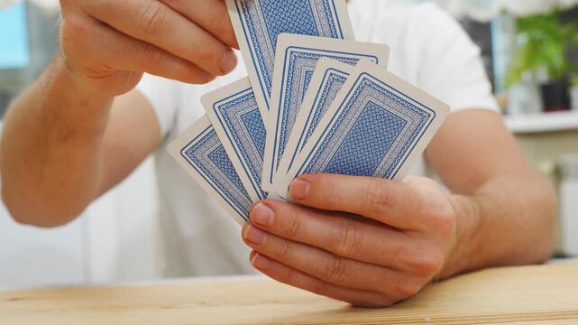 without a face. Hands of a man in a white t-shirt with cards during the game. gambling. A board game for spending leisure time with friends and family.