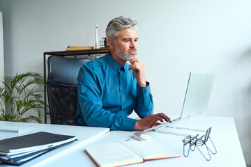 Professional man working thoughtfully at a desk with a laptop in office setting.