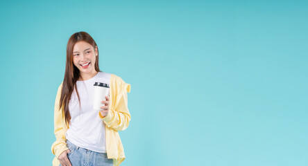 Happy young Asian woman holding a coffee cup while smiling against a blue background, symbolizing...