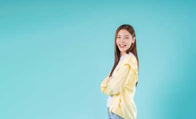 Smiling young Asian woman with crossed arms standing against a blue background, perfect for...