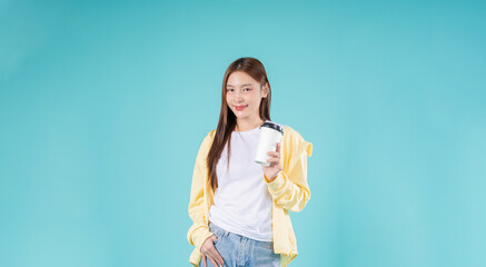 Happy young Asian woman holding a coffee cup while smiling against a blue background, symbolizing...