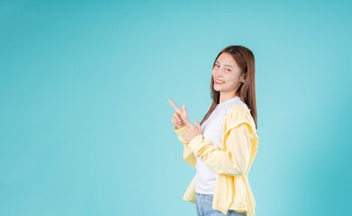Excited young Asian woman pointing to the side with both hands against a blue background, ideal for...