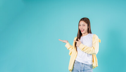 Happy young Asian woman pointing at open hand with a smile against a blue background, perfect for...