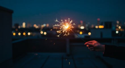Hand holding a glowing sparkler against a blurred city skyline at night, celebrating a festive urban moment