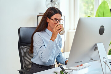 Professional Woman Working At Desk With Computer And Drinking Coffee, Office Environment, Daylight...