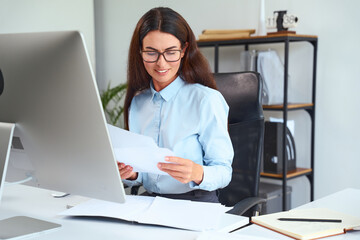 Professional Woman Working At Office Desk, Reviewing Papers, Wearing Glasses And Blue Shirt....