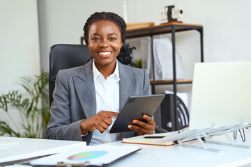 Confident Businesswoman In Formal Attire Smiling In Modern Office With Digital Tablet And Laptop,...