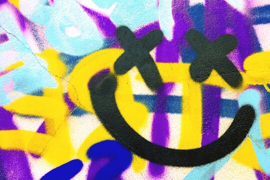 Graffiti smiley face with X eyes in bold yellow, purple, blue. Retro 90s style, vibrant, cartoon graffiti art. Street art, urban design, modern 90s, creative banner, funky visuals.