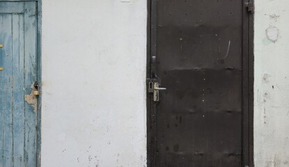 An old brown iron door and a dilapidated blue wooden door serve as the exit to the back of the apartment. Two old, dilapidated doors and a white cement wall.