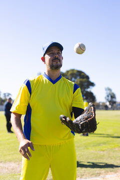Male baseball player standing on grass field under clear sky tossing baseball with glove