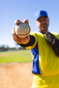Baseball player extending arm holding worn baseball toward camera on pitcher's mound, with glove
