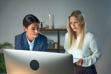Two Professional Women Collaborating In An Office Environment Near A Computer, Showcasing...