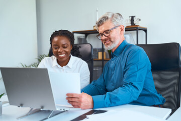 Two colleagues collaborating in an office setting, discussing ideas while viewing documents and a...