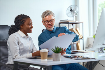 Smiling Professional Colleagues Analyzing Documents at Office Desk While Collaborating on Project...