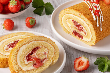 Delicious strawberry roll cake served on a wooden board with fresh strawberries in a white bowl in the background
