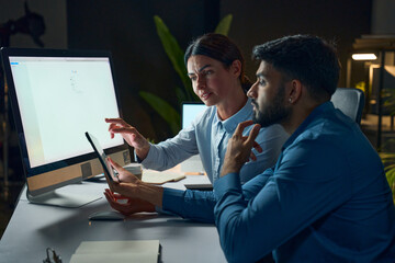 Two Professionals Collaborating In Modern Office Setting While Reviewing Documents On Digital Devices Among Computers, Depicting Teamwork, Focus, And Communication In A Business Context