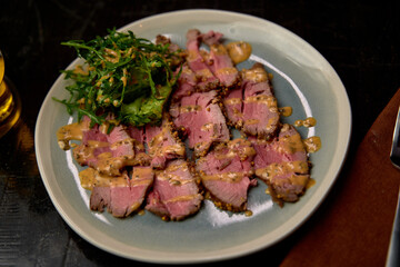 A Delicious Plate of Sliced Roast Meat Garnished with Fresh Greens and Drizzled with Savory Sauce on a Stylish Dinner Table Setting