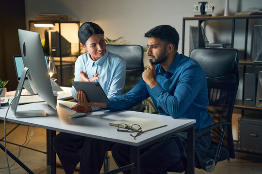 Colleagues Collaborating In A Modern Office, Reviewing Information On A Tablet And Computer. Teamwork, Professional Business Environment, And Creative Problem-Solving.