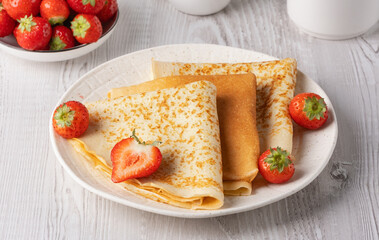 Freshly cooked pancakes with strawberries on a white table