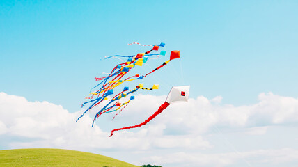 A low-angle photograph of colorful kites flying against a bright blue sky with white puffy clouds