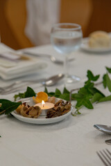 Detail of elegant table decoration at a festive event. Green leaves and a small lit candle create a cozy, natural centerpiece for an inviting celebration.
