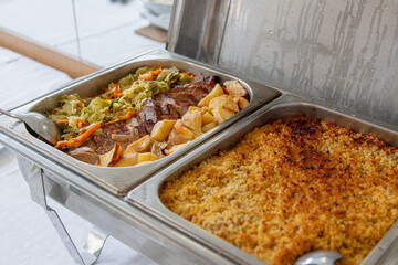 Buffet lunch served at a catered event. Hot chafing dishes feature a meat dish with roasted potatoes and vegetables, and a baked fish dish. Ideal for gatherings.