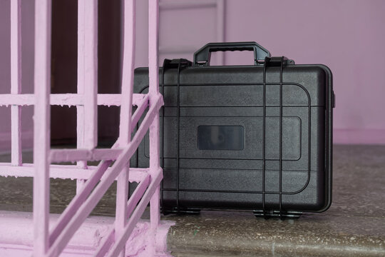 A rugged black protective case rests on a concrete floor next to pink painted metal bars in an old building. Photo