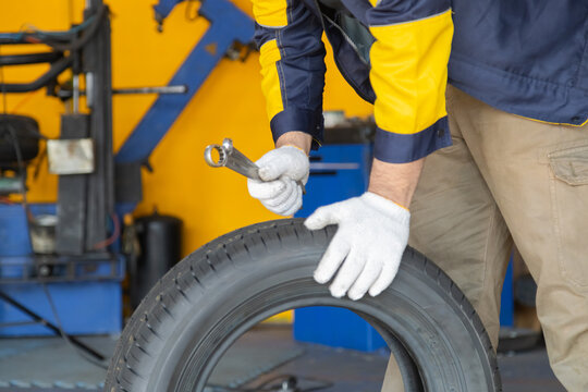 Small business garage, mechanic checks car tire in automotive shop, worker using tool for precision maintenance, showing hands-on skill, professional workshop service, and confidence in repair task
